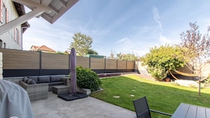 Une terrasse avec des meubles d’extérieur, un espace salon abrité et une cour arrière avec pelouse.
