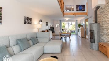 Un salon moderne avec un canapé d’angle, une table à manger avec des chaises, une cheminée et une vue sur l’extérieur.
