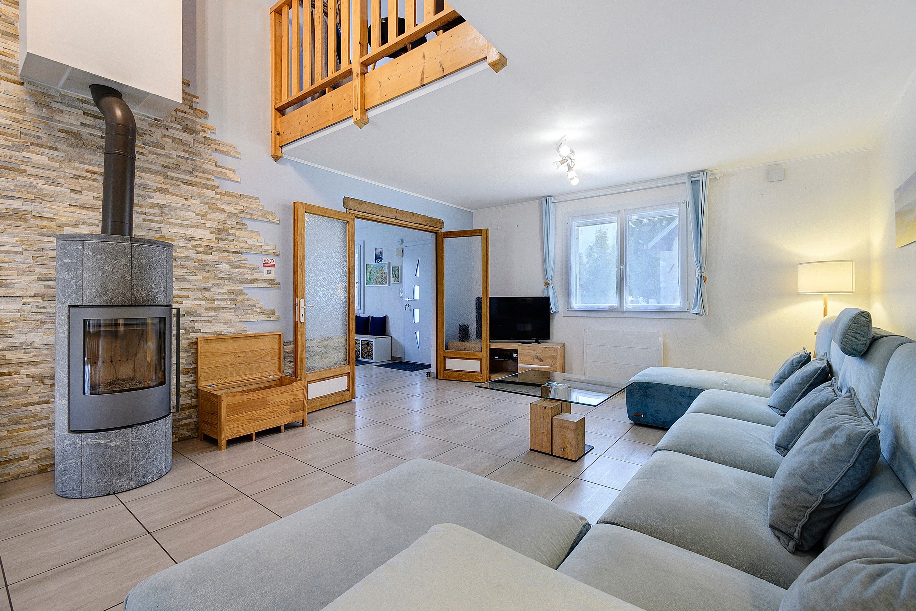 Un salon avec une cheminée en pierre, un escalier en bois, un canapé et un téléviseur.
