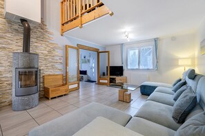 Un salon avec une cheminée en pierre, un escalier en bois, un canapé et un téléviseur.