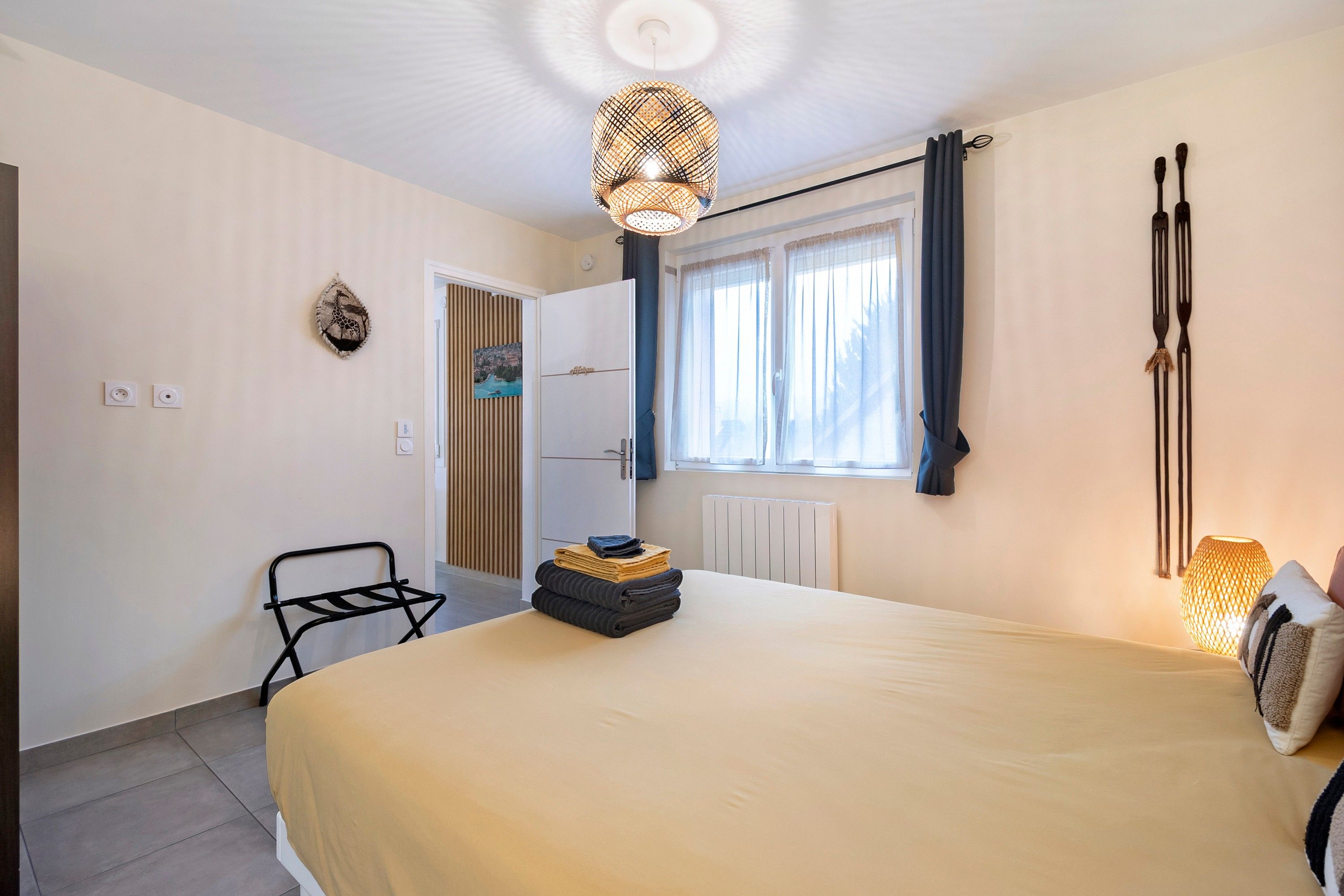 A bedroom with a bed, a chair, a radiator, a window with curtains, a wall-mounted light fixture, and a wall decoration.