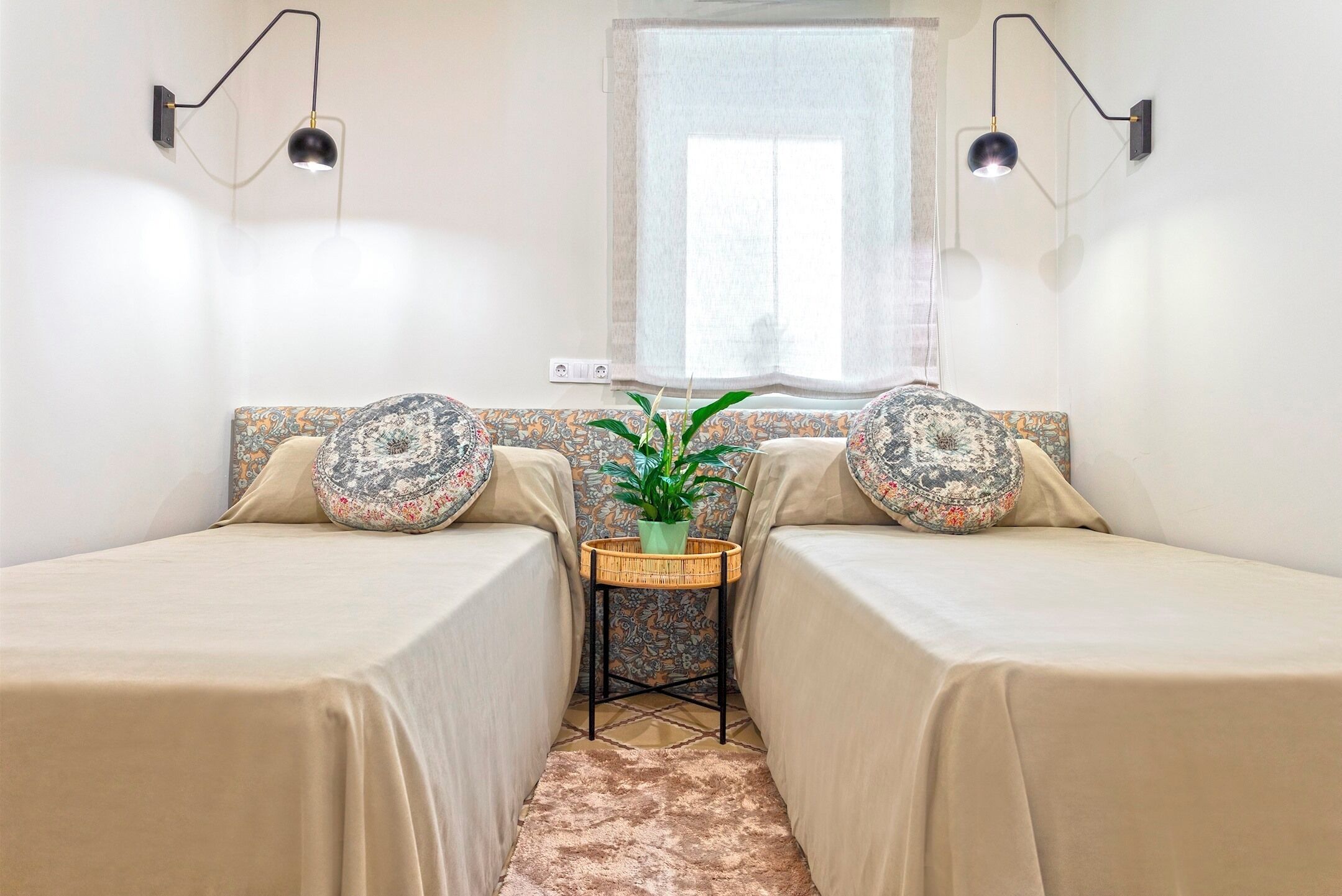 A small, cozy room with two single beds, a small table with a plant, and two wall-mounted lamps.