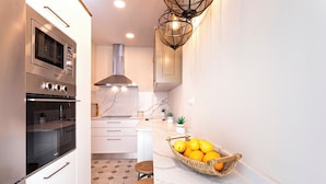 A modern kitchen with a built-in oven, a stainless steel range hood, and a marble countertop. There is a basket of lemons on the counter and a small stool. - Wonderful 5-bedroom Apart in Granada. Recogidas II (Granada)