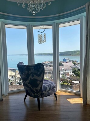 A room with a large bay window, a chair, and a chandelier.
