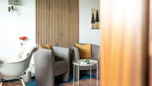 A modern living room with a grey sofa, a white armchair, a small round table with plants, a wooden slat wall, and a framed picture of trees. - Apartment 'Bergluft' with Rhine Valley View, Private Terrace and Wi-Fi (Sasbachwalden)