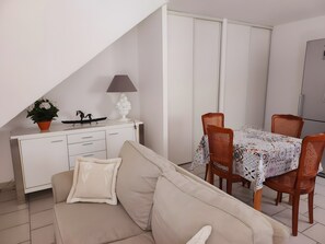 A living room with a sofa, a dining table with chairs, a white cabinet, a lamp, and a potted plant. - Gîte Le Roma with Shared Pool, Wi-Fi, and Air Conditioning in Oppède (Oppède)