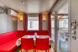 Ein Zimmer mit einem roten Sofa, einem Tisch mit zwei Stühlen, einem Fenster mit Vorhängen und einer Klimaanlage.