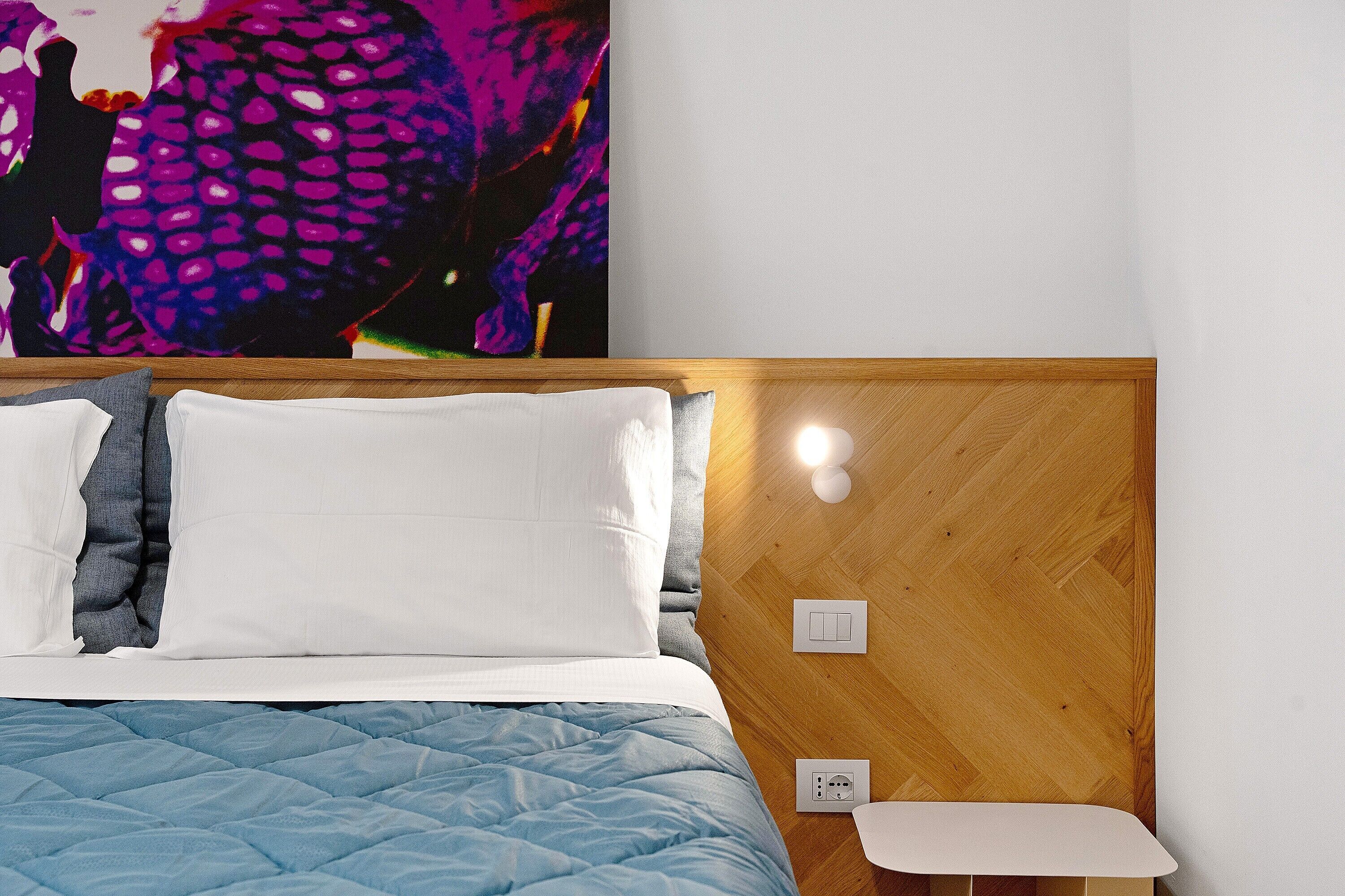 Une chambre à coucher avec une tête de lit en bois, un lit avec des oreillers blancs et gris, une couvre-lit matelassée bleue et une table de chevet blanche.