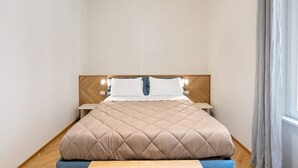A neatly made bed with a quilted headboard, a bedside table with a lamp, and a window with curtains. - Superior Family Apartment with Wi-Fi and Air Conditioning (Napoli)