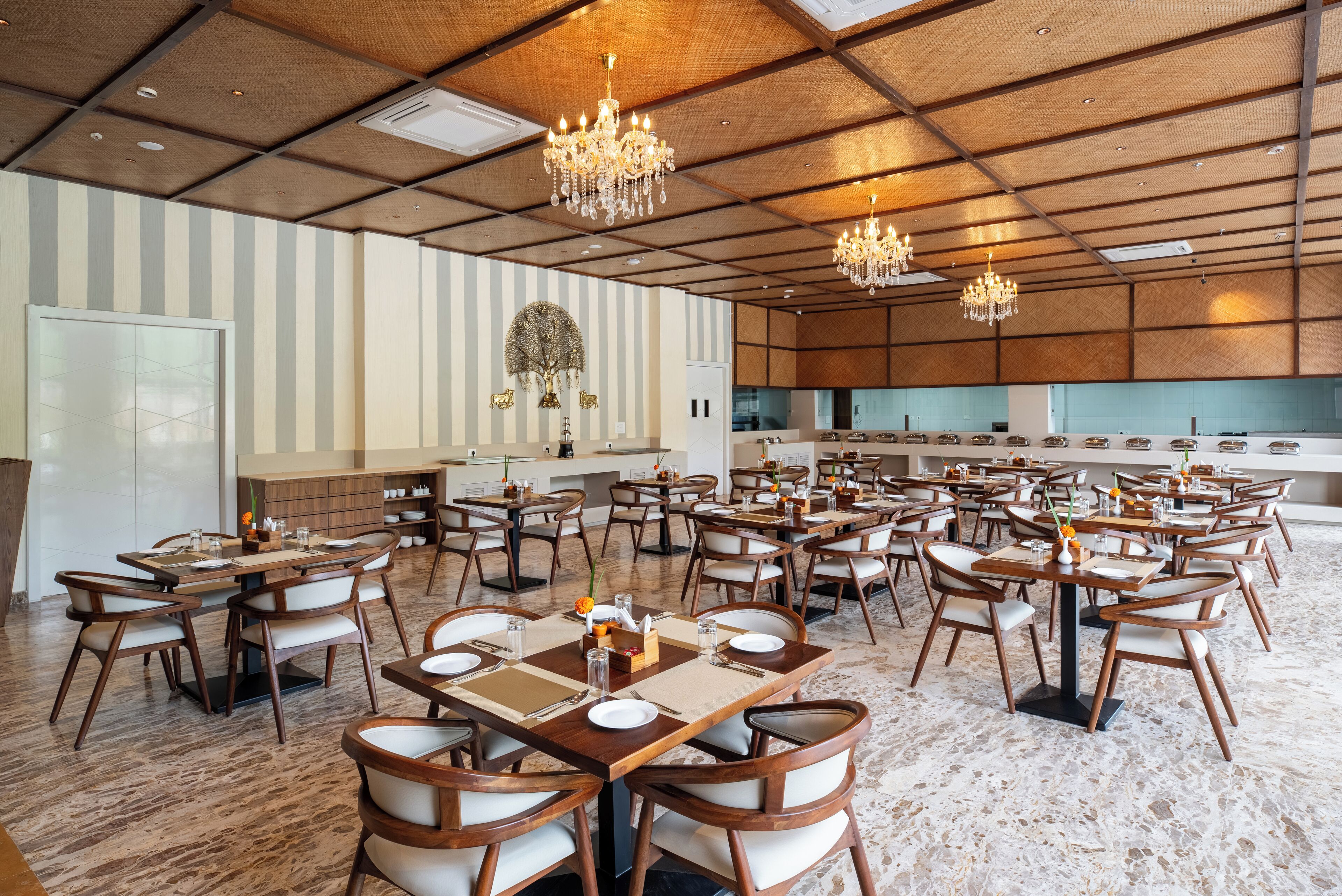 Ampla sala de jantar com várias mesas e cadeiras, cozinha ao fundo e lustres decorativos.