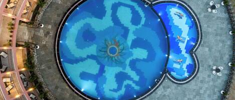 Una piscina circular con una fuente en el centro, rodeada de zonas de descanso y un camino de piedra.