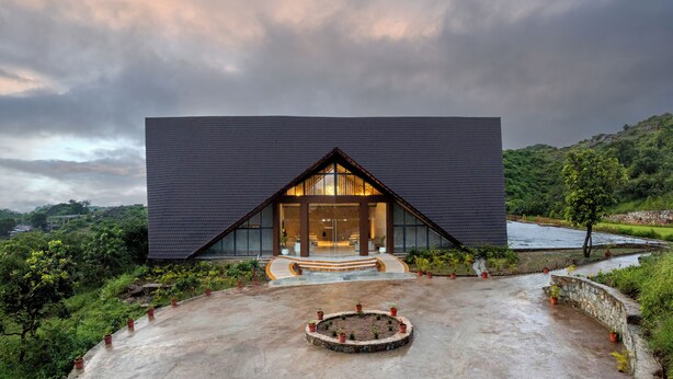 A modern building with a dark roof and large glass windows, surrounded by lush greenery and a circular garden.