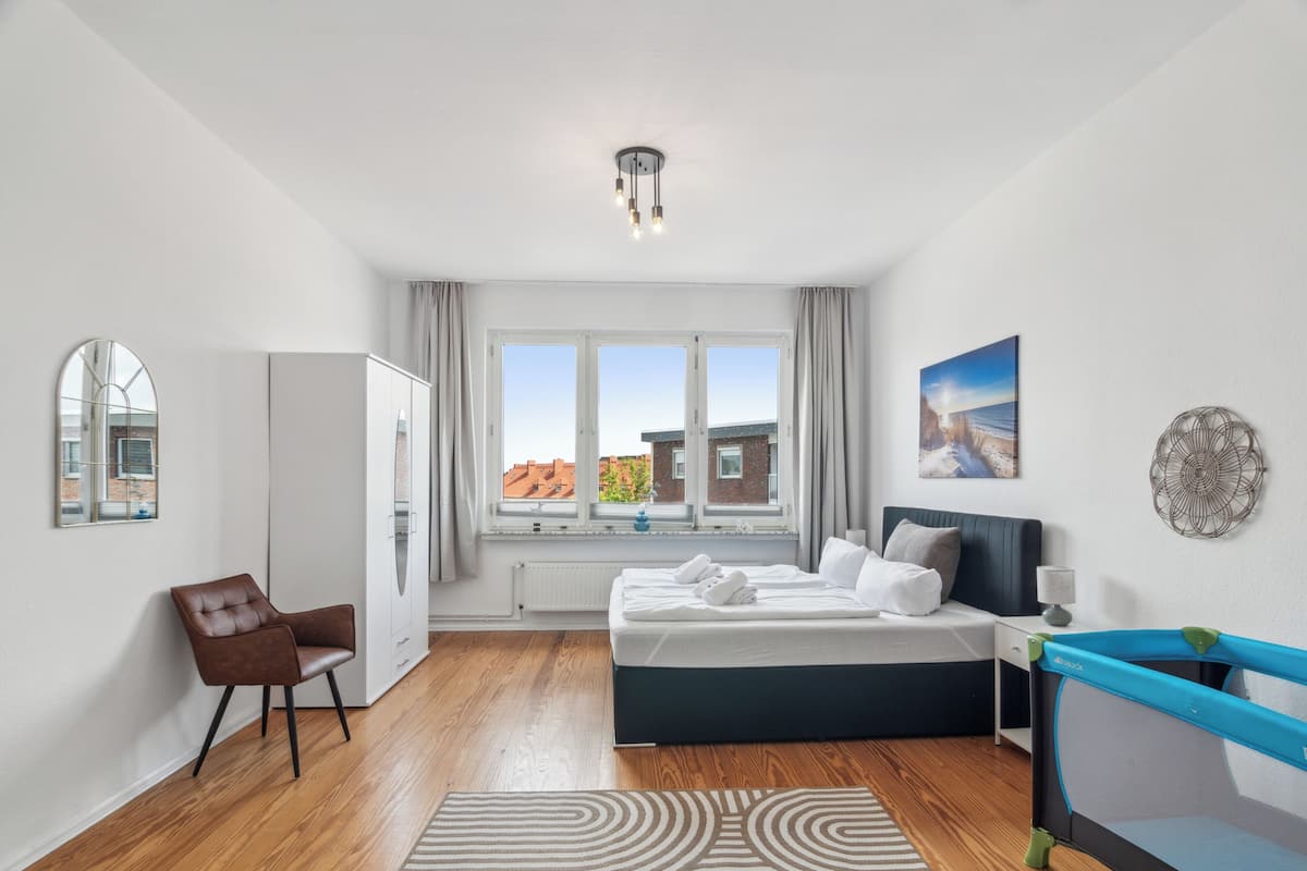 Habitación de hotel moderna con una cama grande, un escritorio, una silla y vistas a edificios a través del ventanal.
