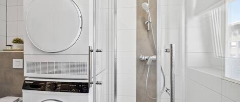 A modern bathroom with a stacked washer and dryer, a glass shower enclosure, and a toilet.
