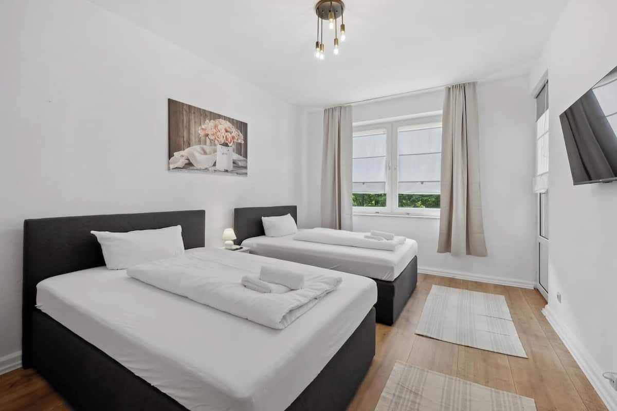Habitación de hotel con dos camas, un ventanal con cortinas, un cuadro en la pared y un televisor de pantalla plana montado en la pared.