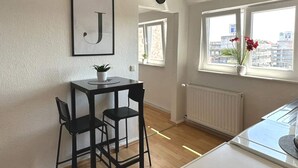 Een moderne keuken met een zwarte tafel en stoelen, een groot raam met uitzicht op de stad, en een lijst met de letter 'J' aan de muur.