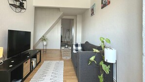 Een moderne woonkamer met een flatscreen televisie, een grijze bank, een kamerbreed tapijt en een trap naar een andere ruimte.