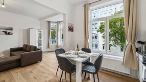 A modern apartment with a dining area, a sofa, and a view of the city. - Infinity Stay Ferienapartments Rheinstrasse (Wilhelmshaven)