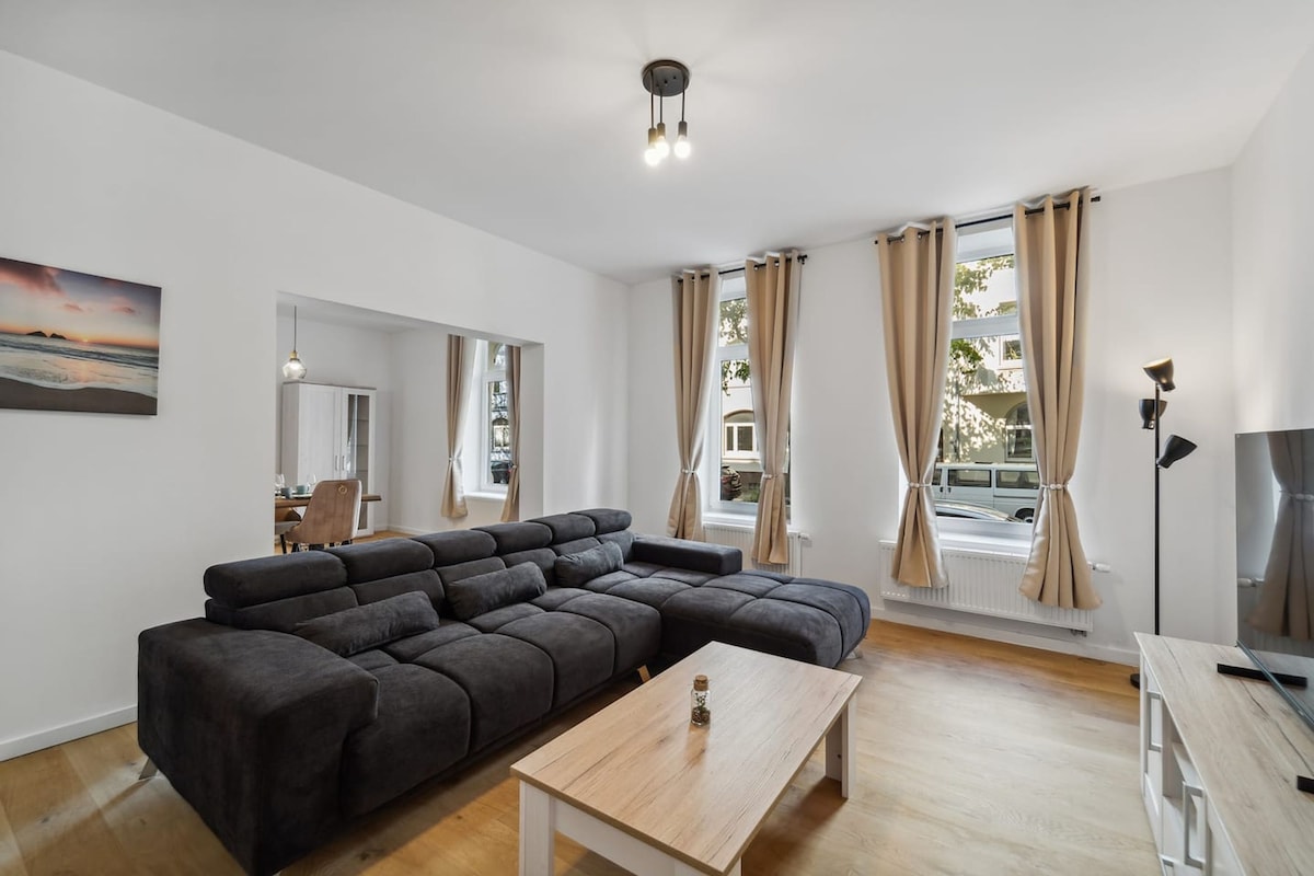 A modern living room with a sectional sofa, a wooden coffee table, and a dining area with a chair and table.