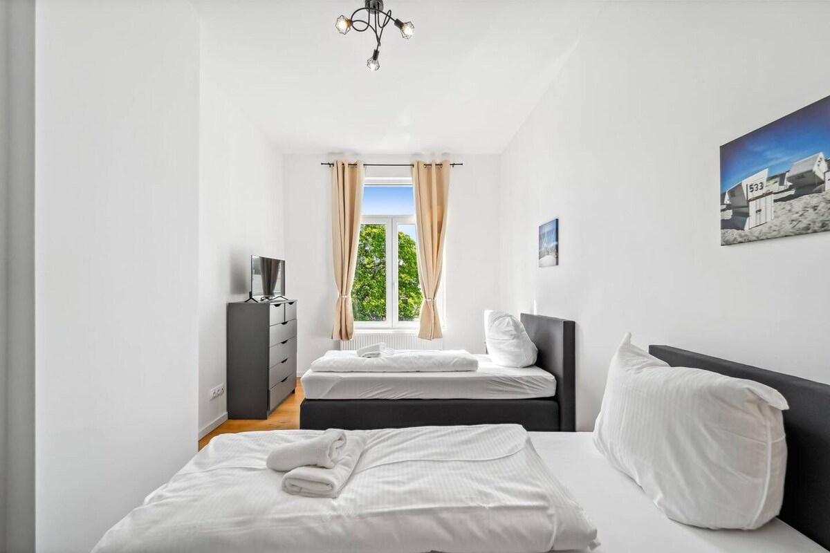 Une chambre avec deux lits, une commode, un téléviseur et une fenêtre avec des rideaux.