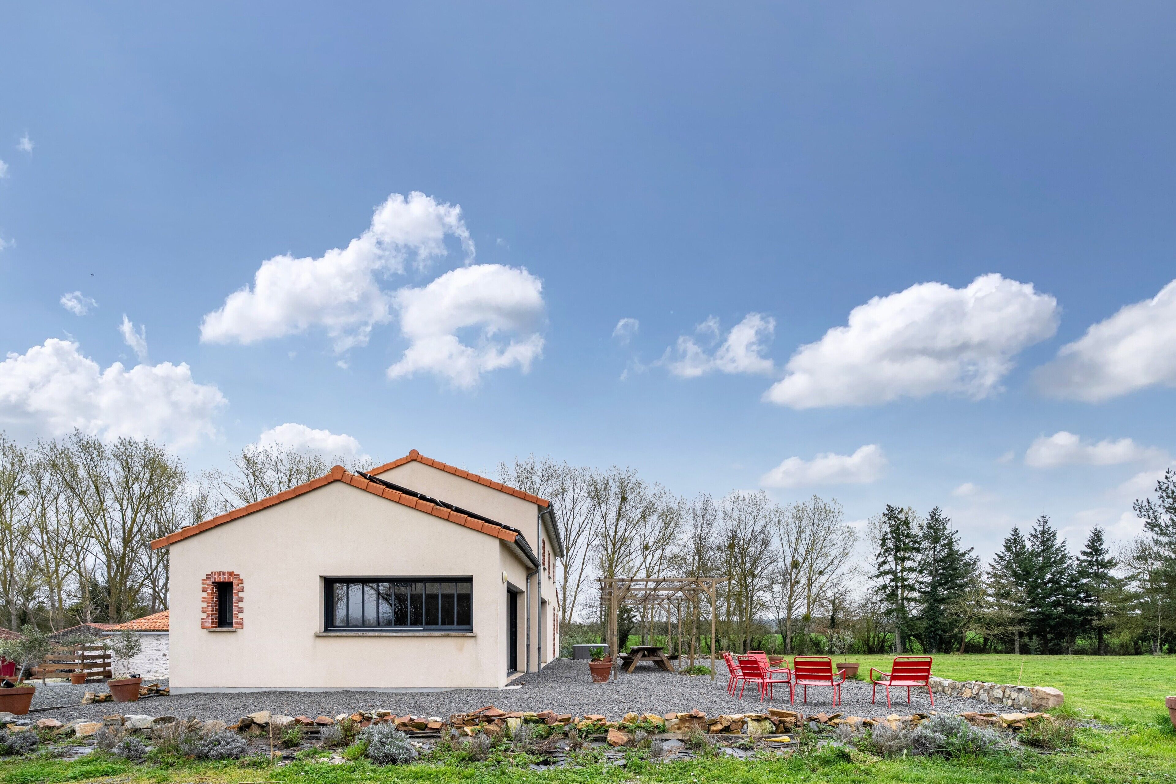 A modern house with a tiled roof, a patio with red chairs, and a stone wall.