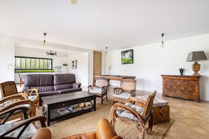 Un salon comprenant un canapé, des fauteuils, une table basse, une table de billard et un meuble.