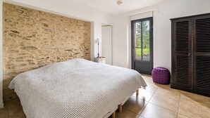 A bedroom with a stone wall, a bed, a door to a balcony, and a wardrobe.