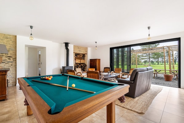 Une table de billard dans une pièce avec une cheminée, un coin repas et une vue sur l’extérieur.