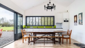 A modern kitchen with a dining table, chairs, a chandelier, and a large window.