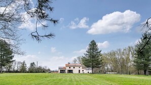 A house with a large lawn, a clear sky, and surrounding trees.