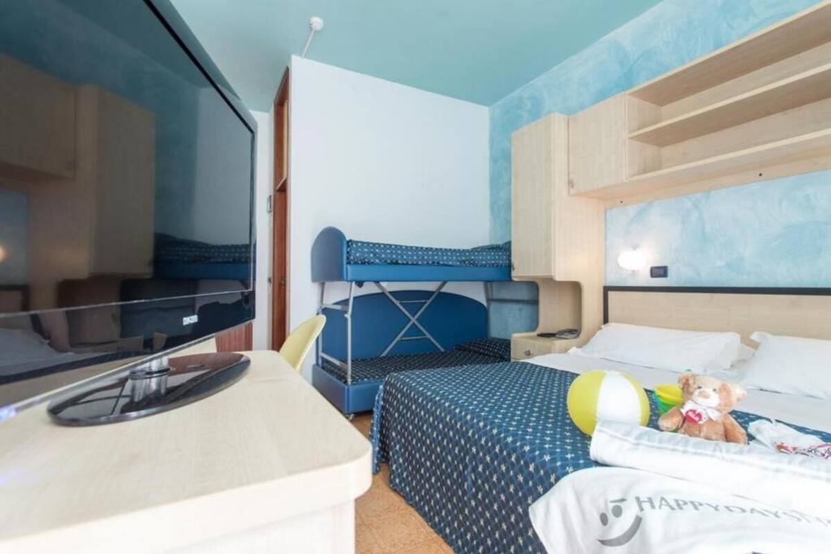 A hotel room with bunk beds, a desk with a computer, and a teddy bear on the bed.