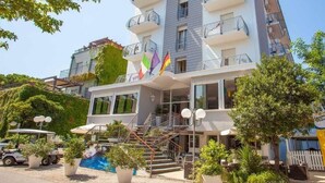 A multi-story hotel with balconies, a swimming pool, and outdoor seating. - Hotel New Castle (Cesenatico)