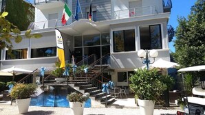 A hotel with a pool, outdoor seating, and multiple flags. - Hotel New Castle (Cesenatico)