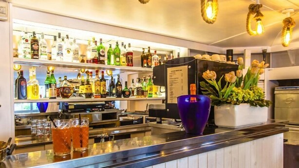 A bar area with shelves of various liquor bottles, a purple glass vase, and a menu board. - Hotel New Castle (Cesenatico)
