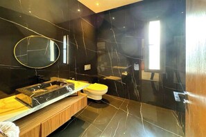 Ein modernes Badezimmer mit schwarzem Marmor an der Wand, einem Holzbadezimmer-Möbel und einer gelben Toilette sowie einem Spiegel.