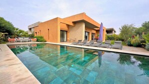 A modern building with a swimming pool, lounge chairs, and a garden area. - Villa Majestueuse - Luxury, Heated Pool & Jacuzzi in Marrakech (Marrakech)