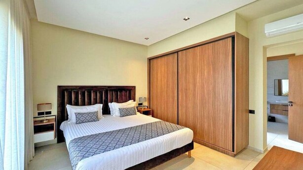 A modern bedroom with a large bed, wooden wardrobe, and a bathroom visible through an open door. - Villa Majestueuse - Luxury, Heated Pool & Jacuzzi in Marrakech (Marrakech)
