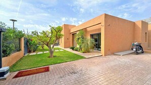 A modern building with a flat roof, a paved driveway, and a small garden area with a tree and shrubs. - Villa Majestueuse - Luxury, Heated Pool & Jacuzzi in Marrakech (Marrakech)