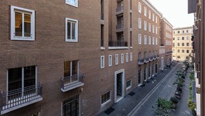 Un edificio in mattoni con diversi piani, balconi, una strada stretta e alcuni passanti.