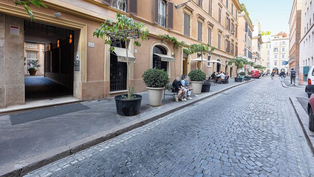 Una strada acciottolata fiancheggiata da edifici storici, tavoli all'aperto e piante in vaso.