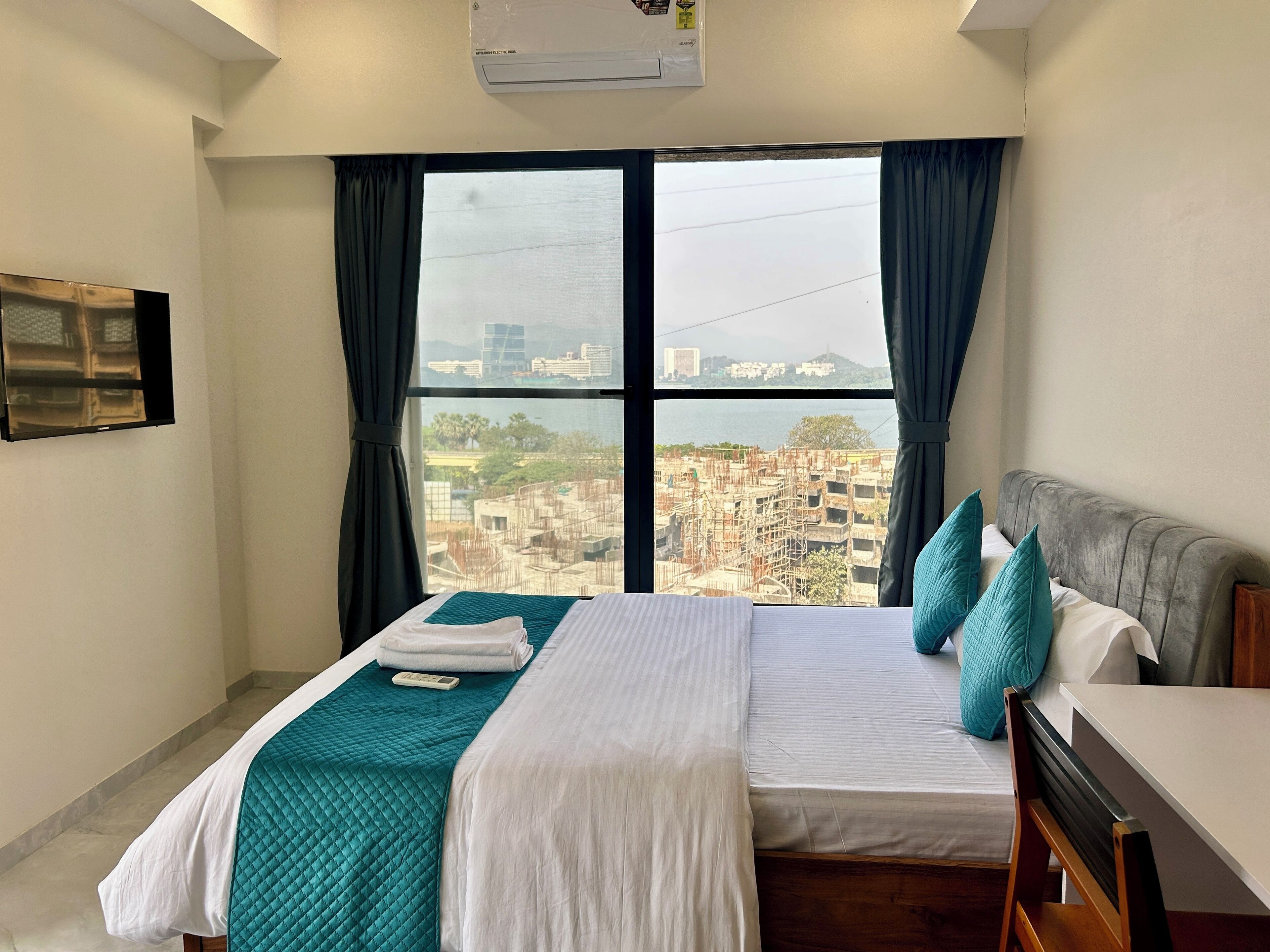 Ein Hotelzimmer mit Bett, Schreibtisch und großem Fenster mit Blick auf die Stadt.