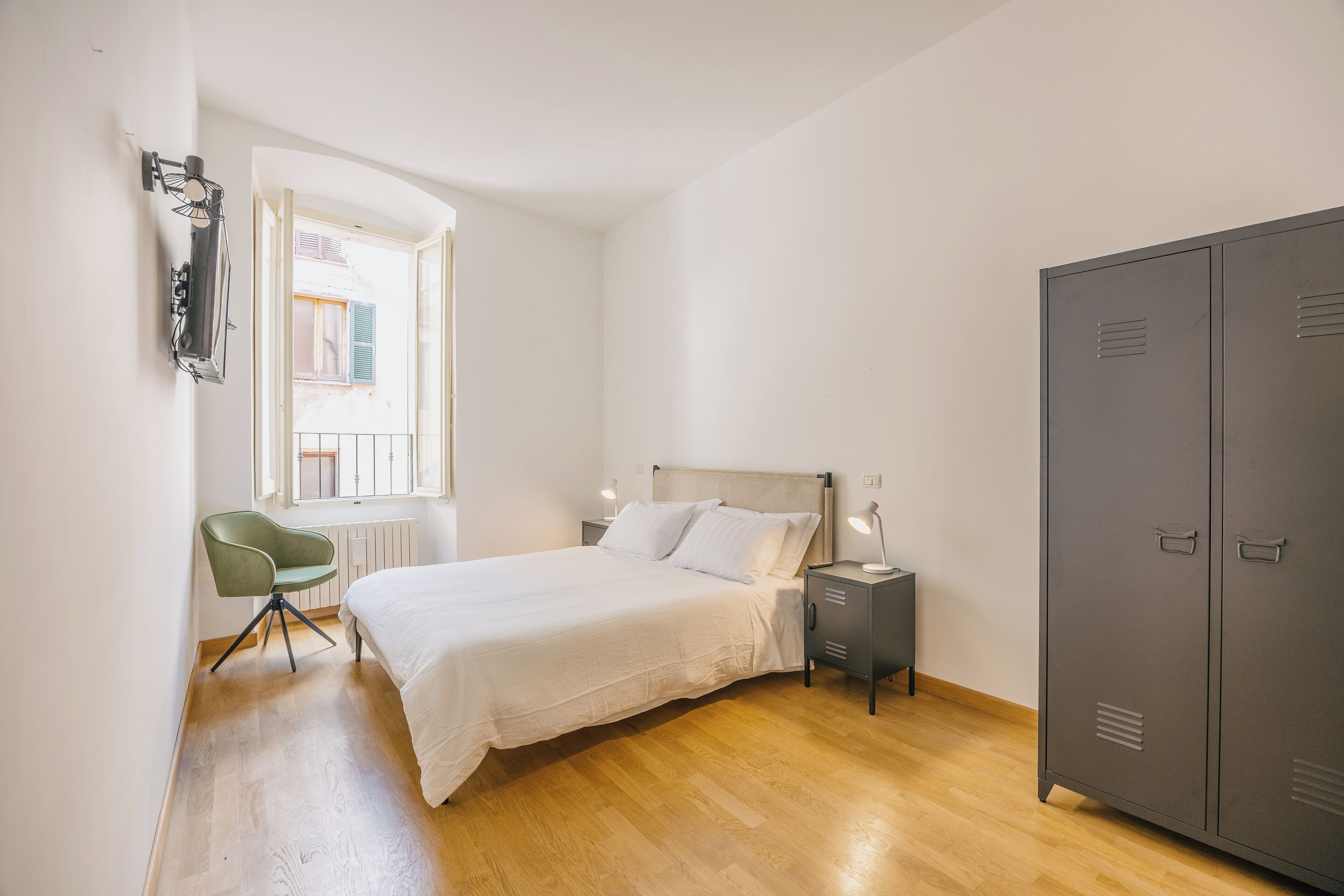 A bedroom with a bed, a desk, a chair, a wardrobe, and a window with a view.