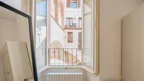 A narrow hallway with a window leading to a courtyard. A radiator is visible below the window, and a small table with a candle holder is placed against the wall. - BHR - The Window on Spoleto (Spoleto)