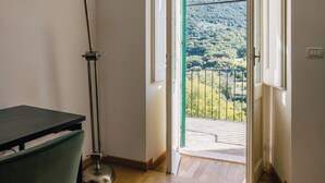 A room with a wooden floor, a desk, a lamp, and an open door leading to a balcony with a view of a hilly landscape. - BHR - The Window on Spoleto (Spoleto)