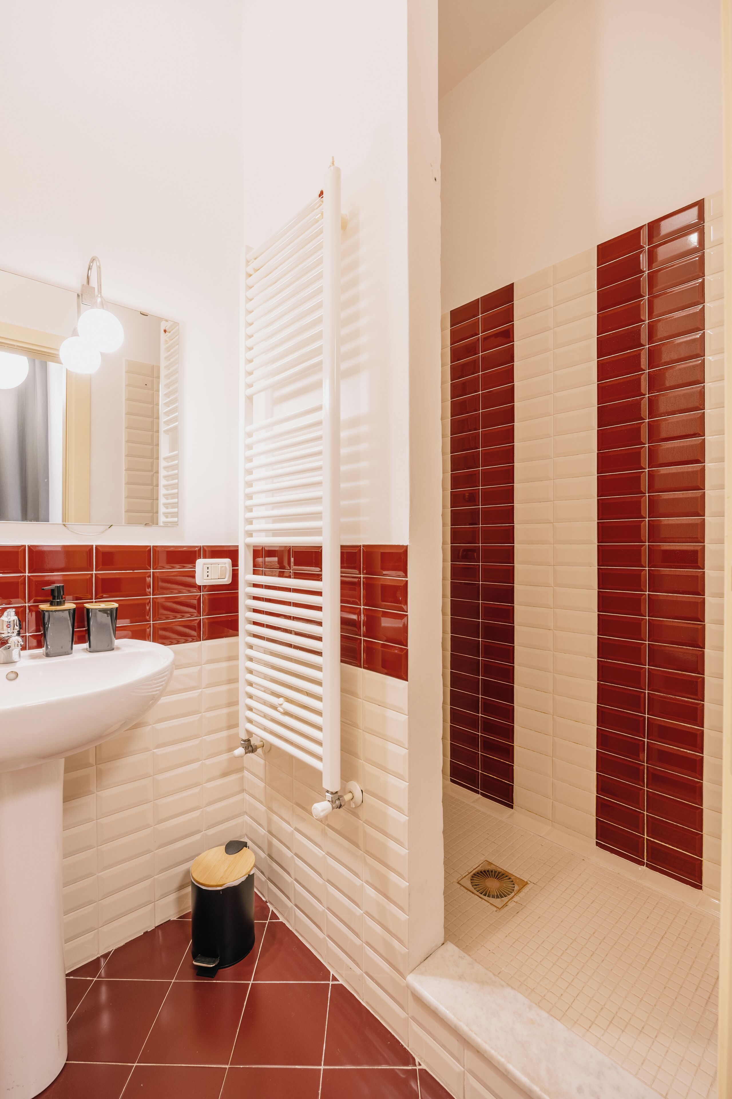 A bathroom with a white sink, mirror, and red-tiled shower enclosure.