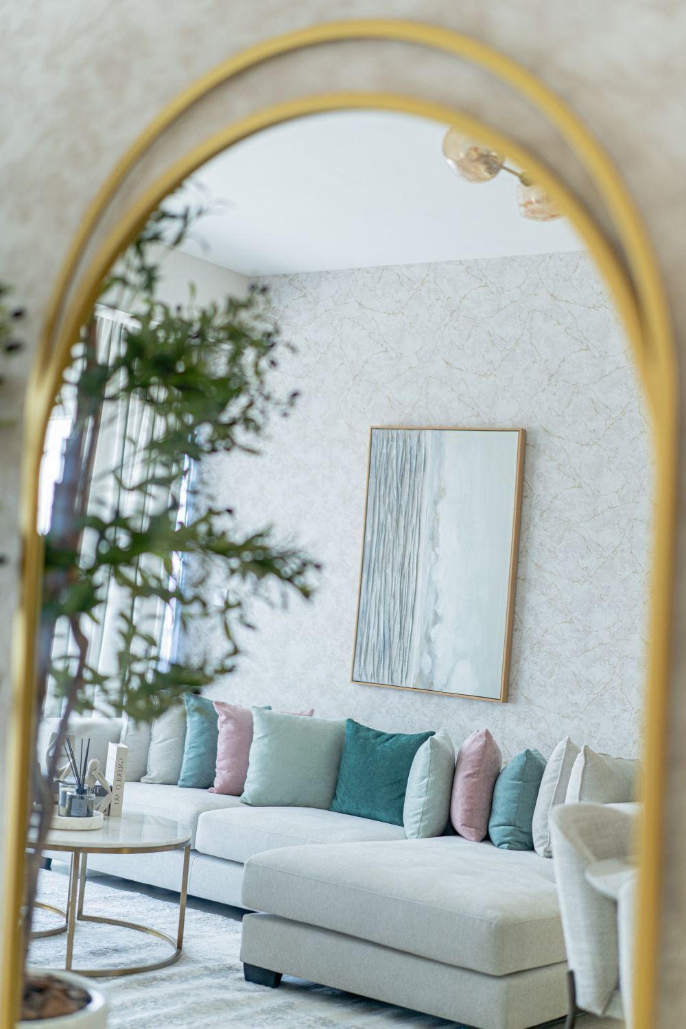 Una sala de estar moderna con un sofá blanco, cojines coloridos, una pared de mármol y un espejo grande.