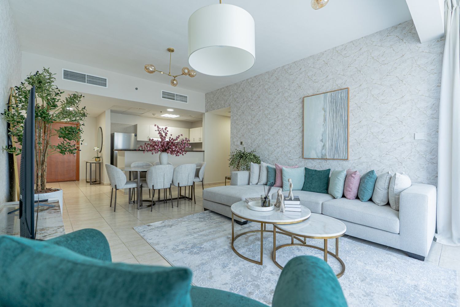 A modern living room with a sofa, coffee table, and chairs. There is a dining area with a table and chairs, and a kitchen in the background.