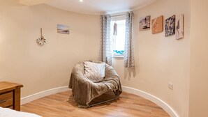 A cozy bedroom with a curved ceiling, a wooden floor, a bed, a chair, and a window with curtains. - Modern ground floor apartment, near the beach (Ceredigion)