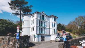 A white multi-story building with a stone wall and a clear blue sky. - Modern ground floor apartment, near the beach (Ceredigion)