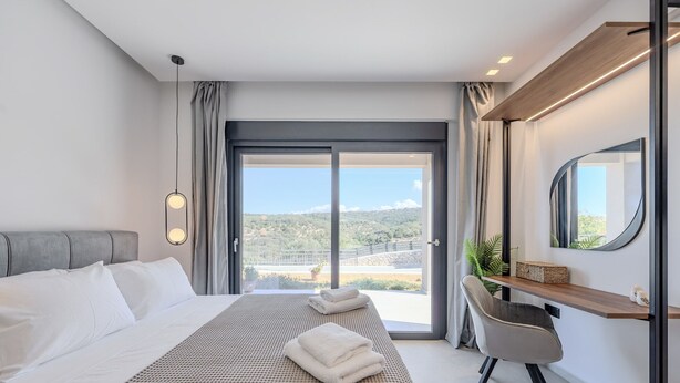 A modern hotel room with a large bed, a desk, and a view of the outdoors. - Villa Allargo - with Private Pool (Gerani)